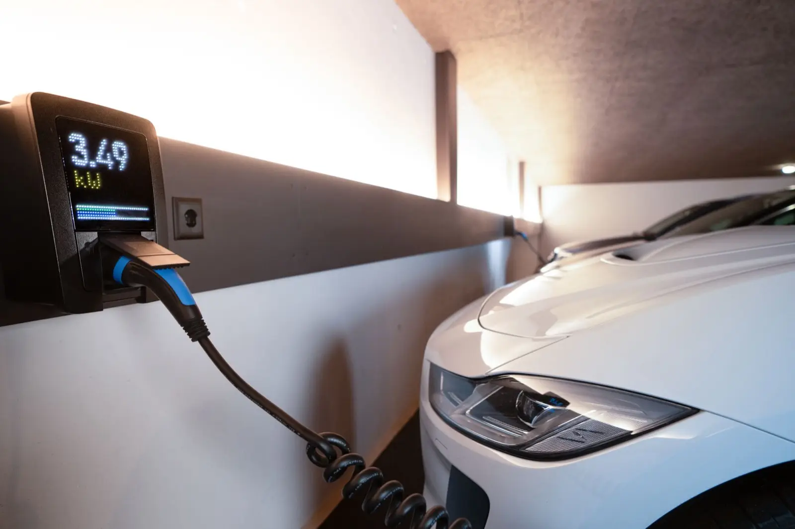 Wallbox an der Garagenwand lädt ein weißes E-Auto