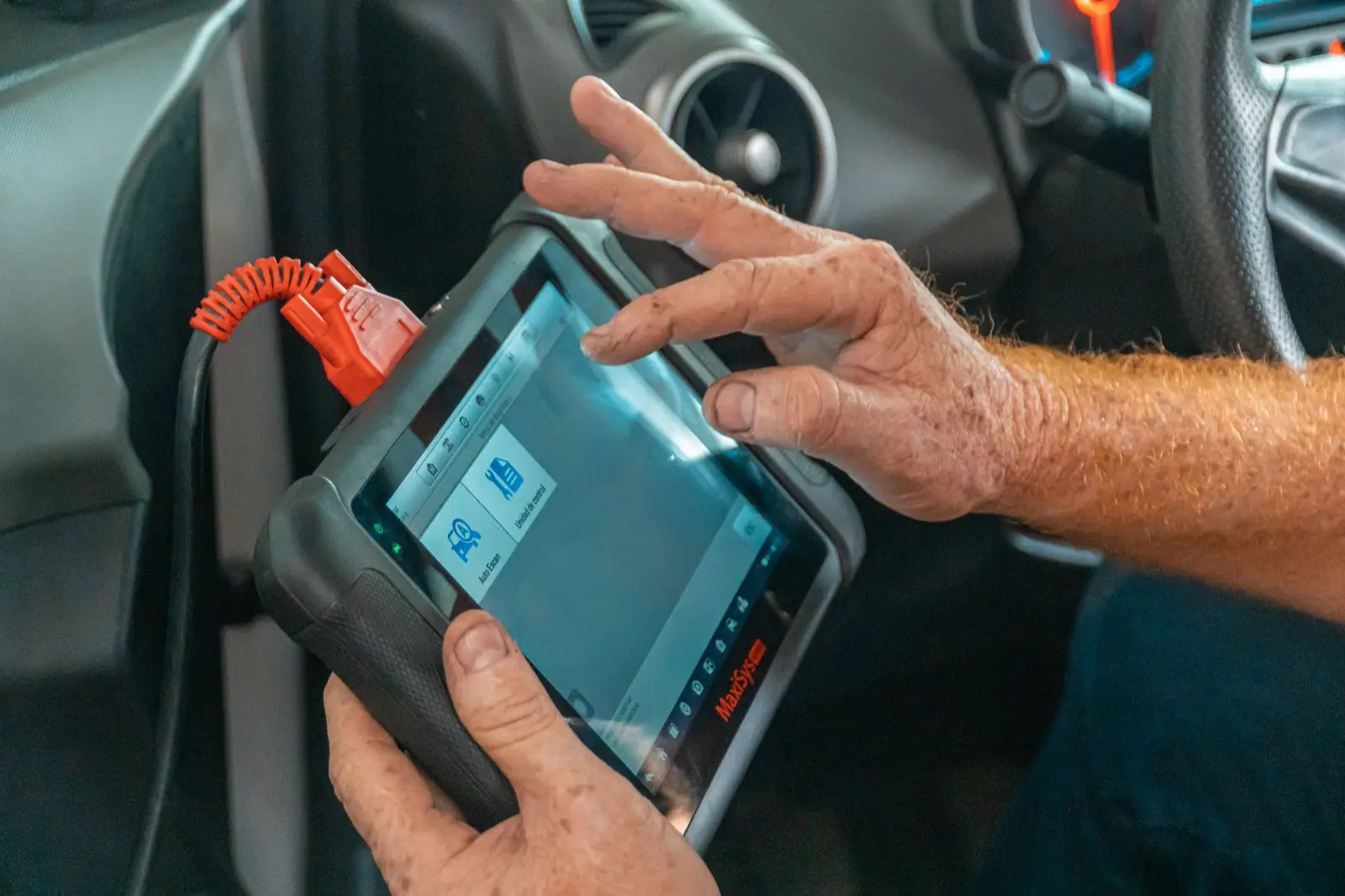 Hände halten ein Diagnosegerät, das per Kabel mit dem Auto verbunden ist