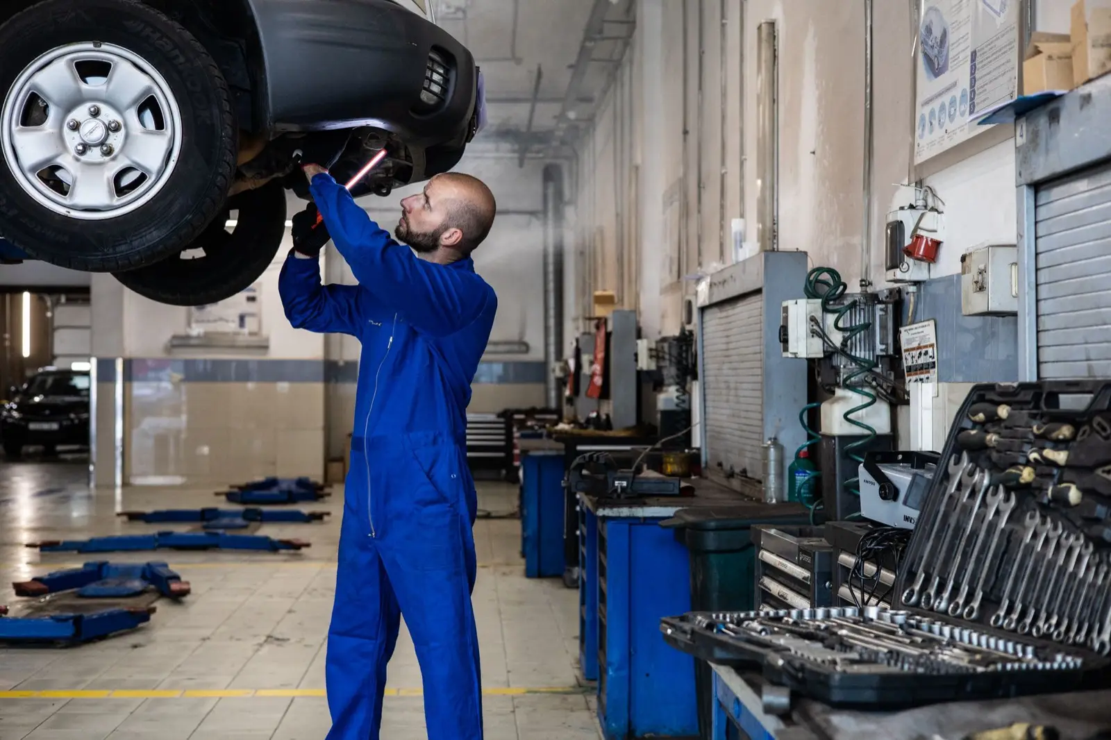 Mechaniker im blauen Overall arbeitet unter einem Auto auf der Hebebühne