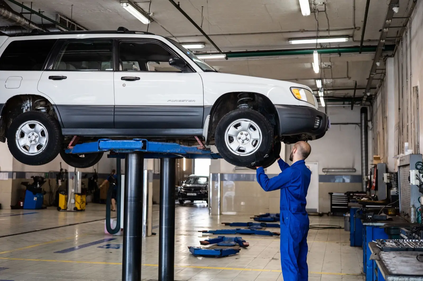 Mechaniker prüft ein Auto auf der Hebebühne in einer hellen Werkstatthalle