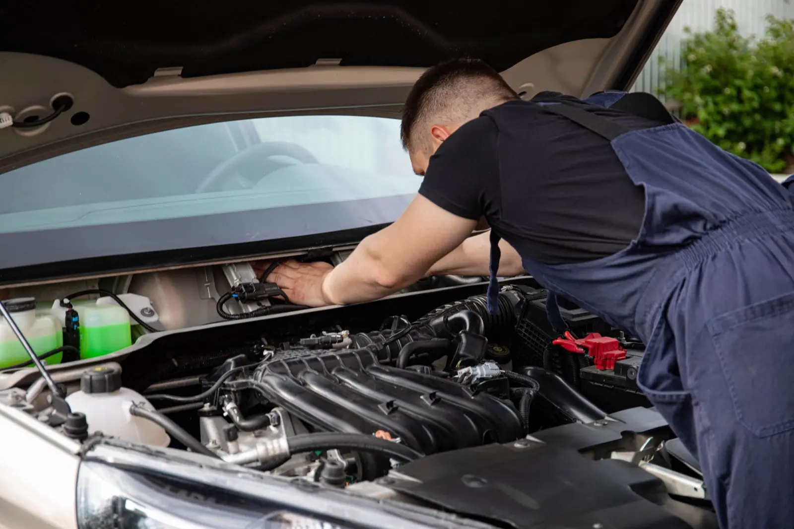 Mechaniker arbeitet im offenen Motorraum eines hellen Autos