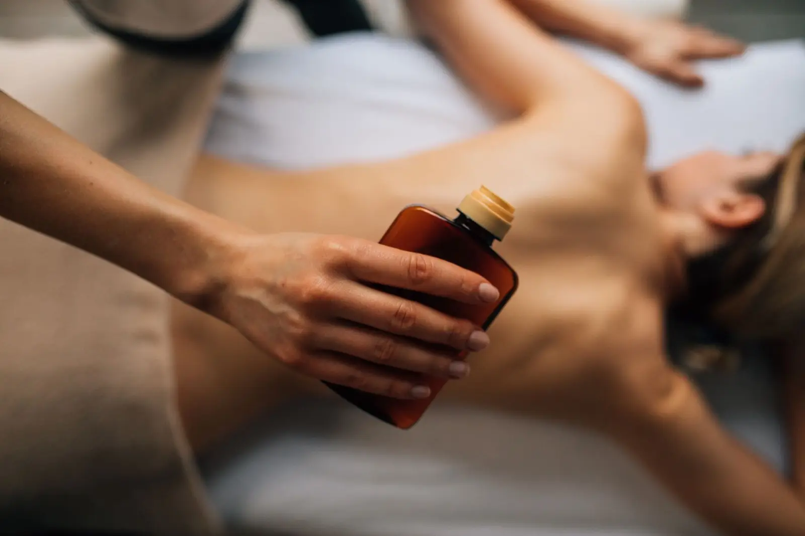 Masseurin gibt Massageöl aus einer braunen Flasche in die Hand