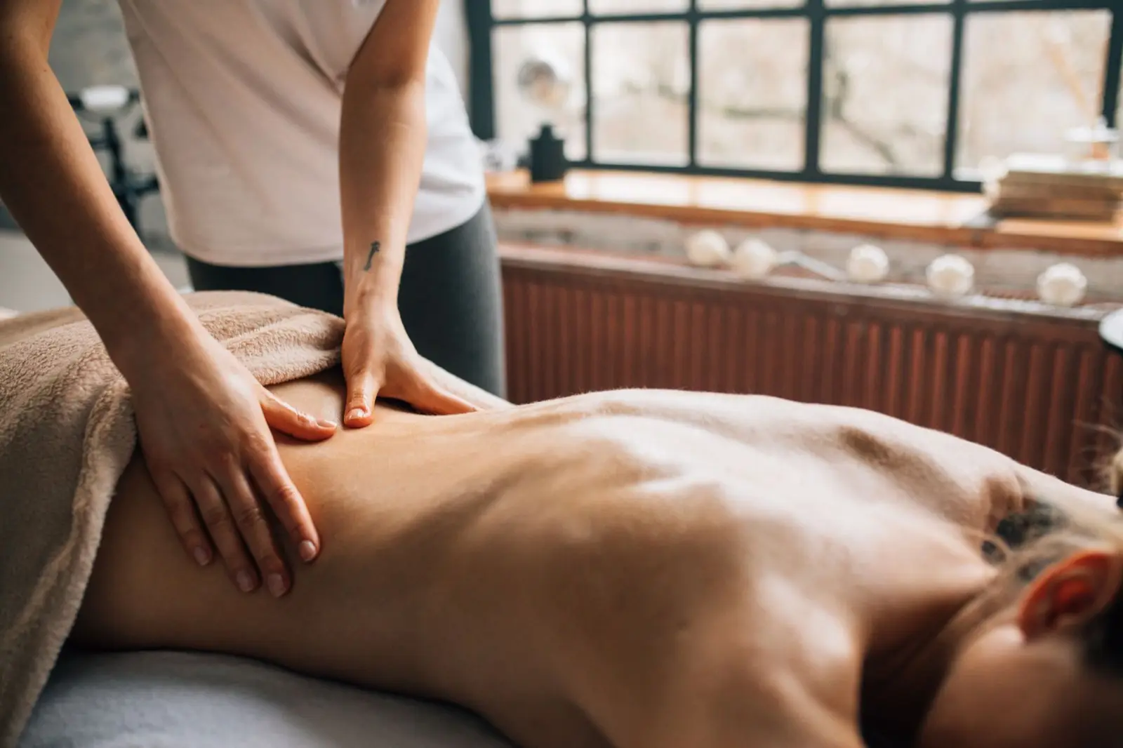 Masseurin massiert mit beiden Händen den Rücken einer Frau auf der Liege