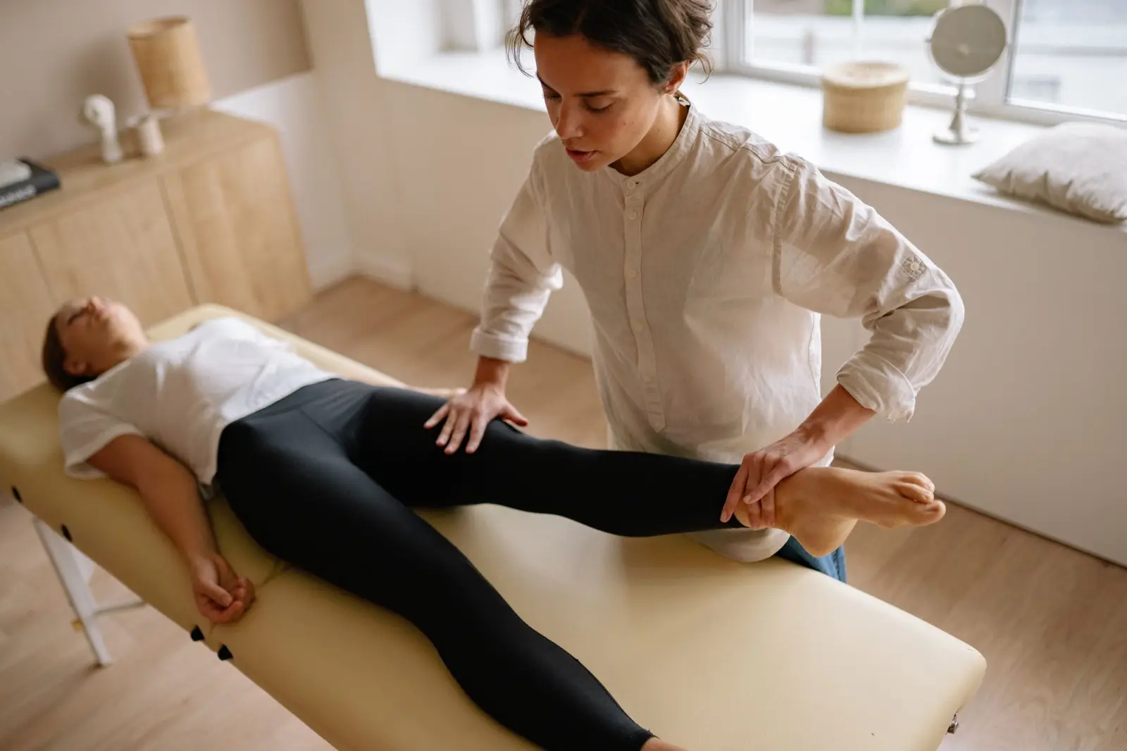 Masseur dehnt das Bein einer Frau auf der Massageliege