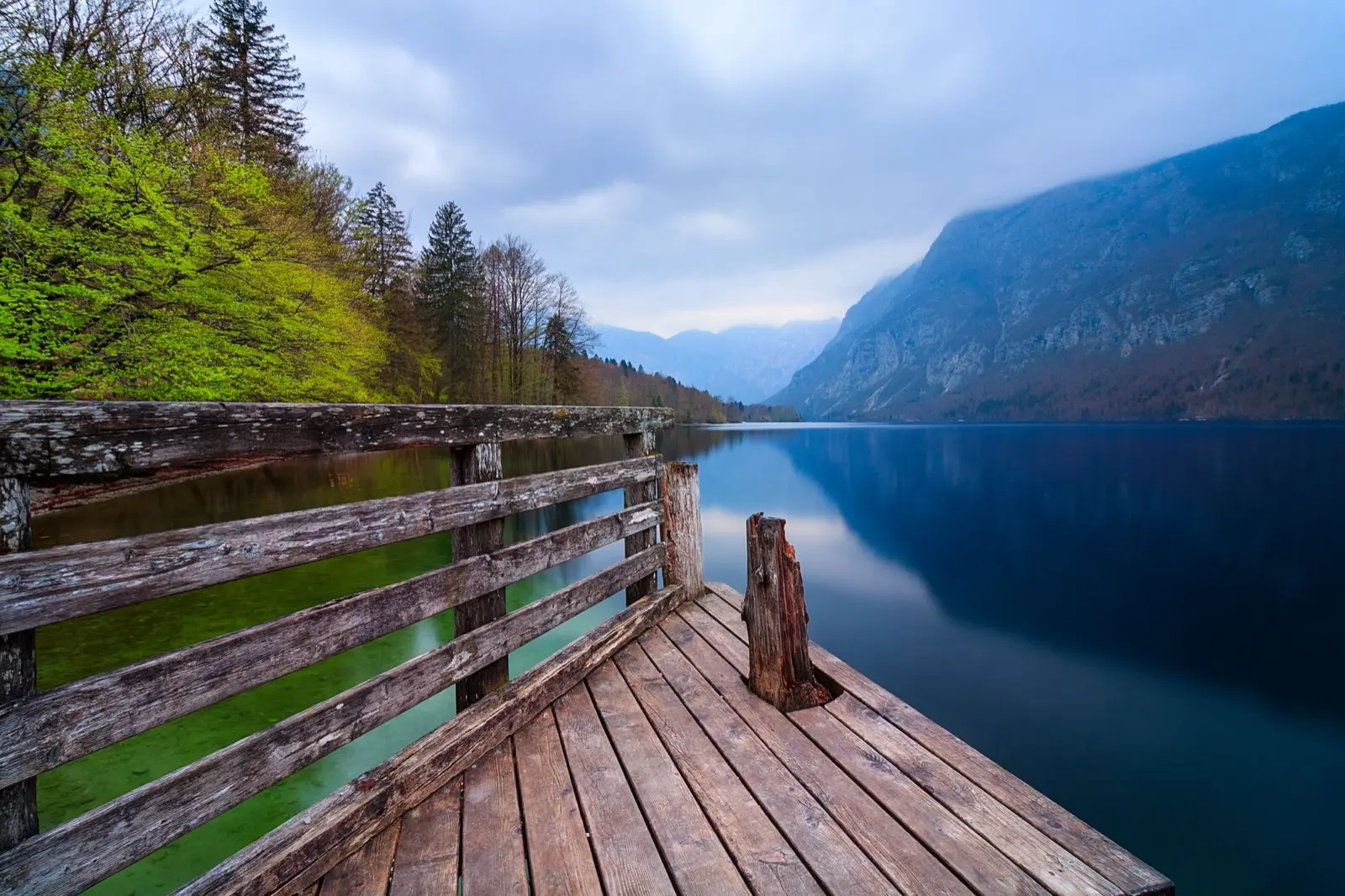 Holzsteg an einem stillen Bergsee, im Hintergrund bewaldete Hänge