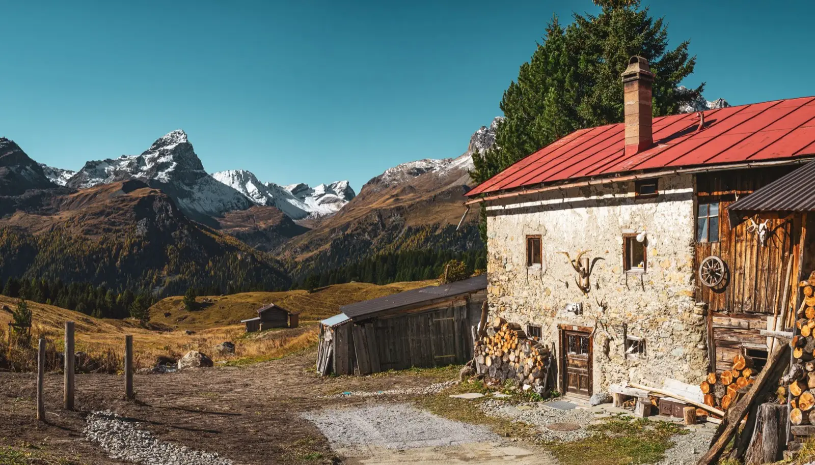Altes Tiroler Bauernhaus mit rotem Blechdach und Rauchfang vor schneebedeckten Bergen