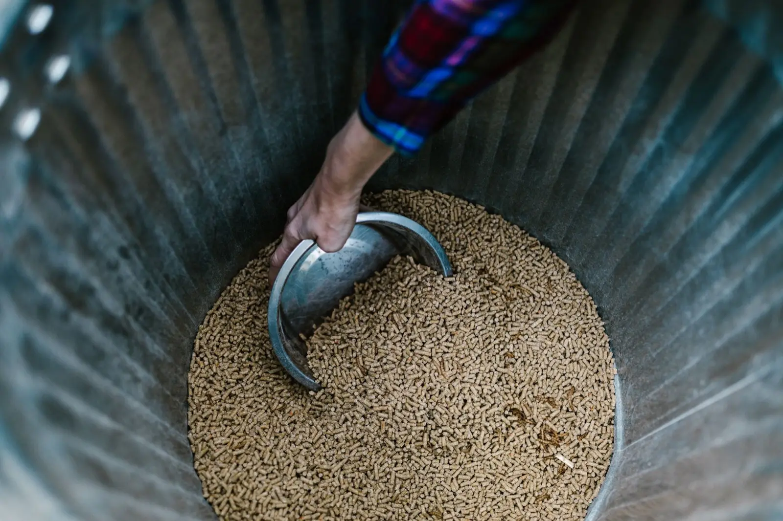 Hände füllen Holzpellets mit einer Schaufel aus einem Metallbehälter