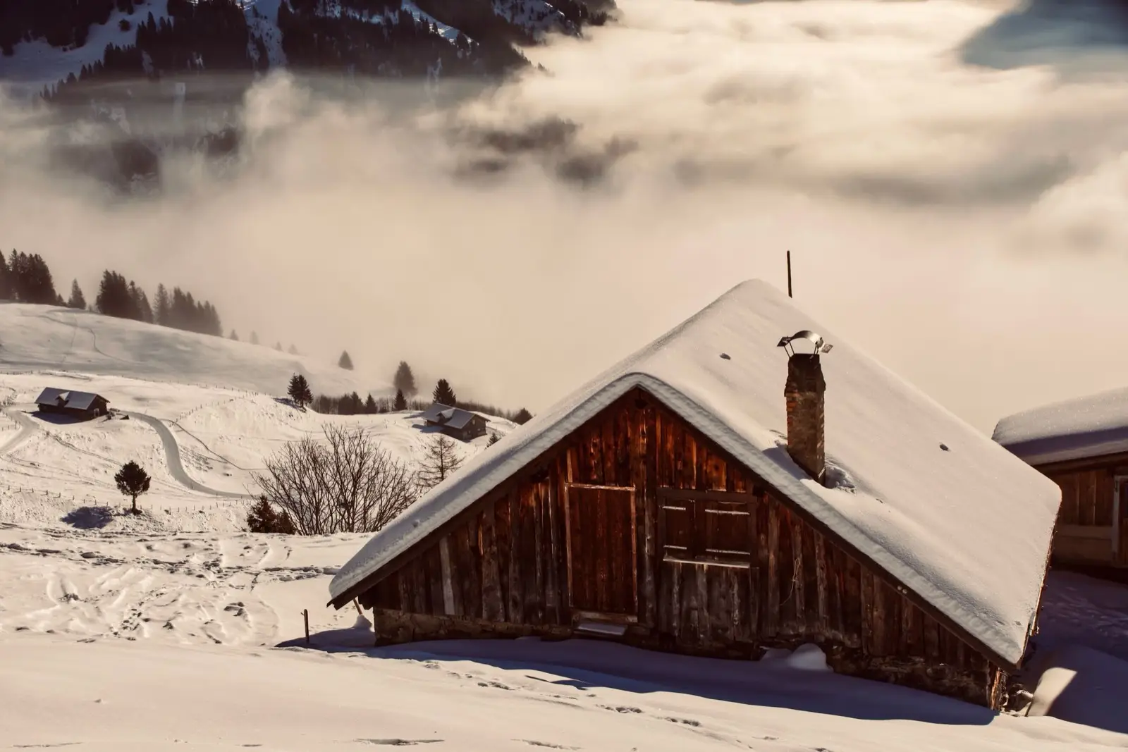 Verschneite Holzhütte mit gemauertem Rauchfang in einer Winterlandschaft
