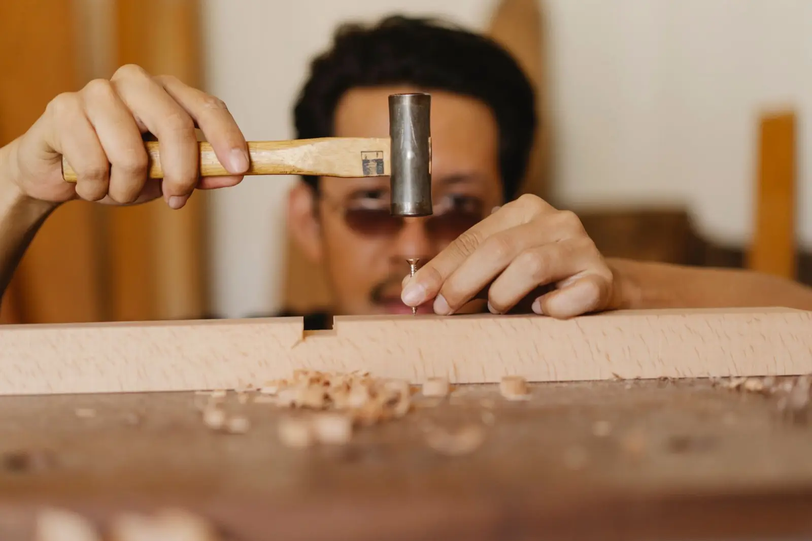 Tischler beim Nageln einer Holzverbindung, konzentriert mit Brille