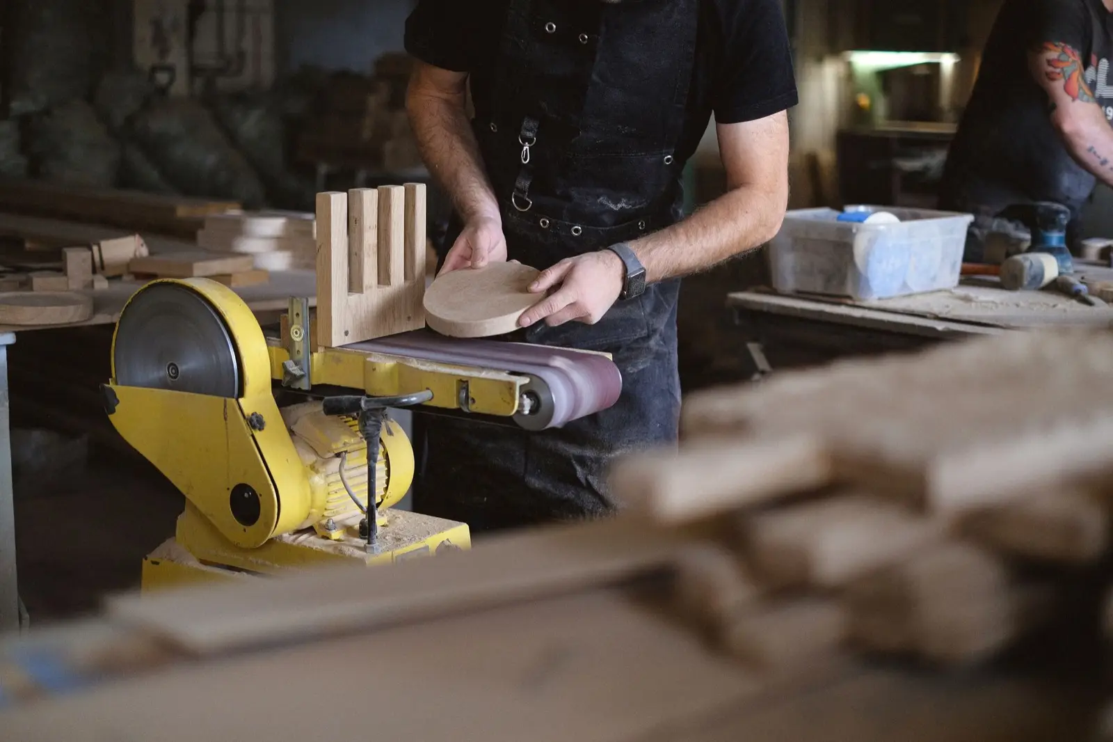 Tischler schleift ein rundes Holzteil an der Bandschleifmaschine