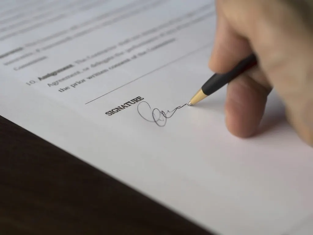 Nahaufnahme einer Hand, die mit einem Kugelschreiber einen Vertrag auf Papier unterschreibt